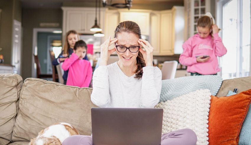 A woman sitting on a couch with her children and dog looking at her laptop.