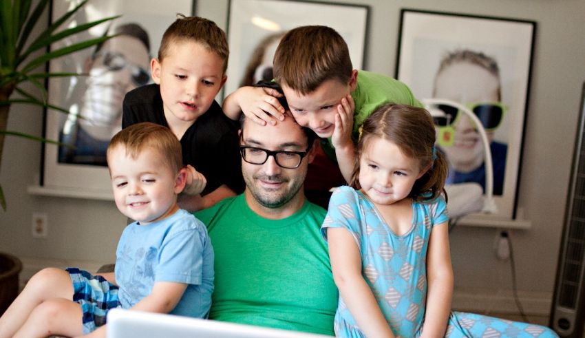 A man and his children are sitting on a couch looking at a laptop.