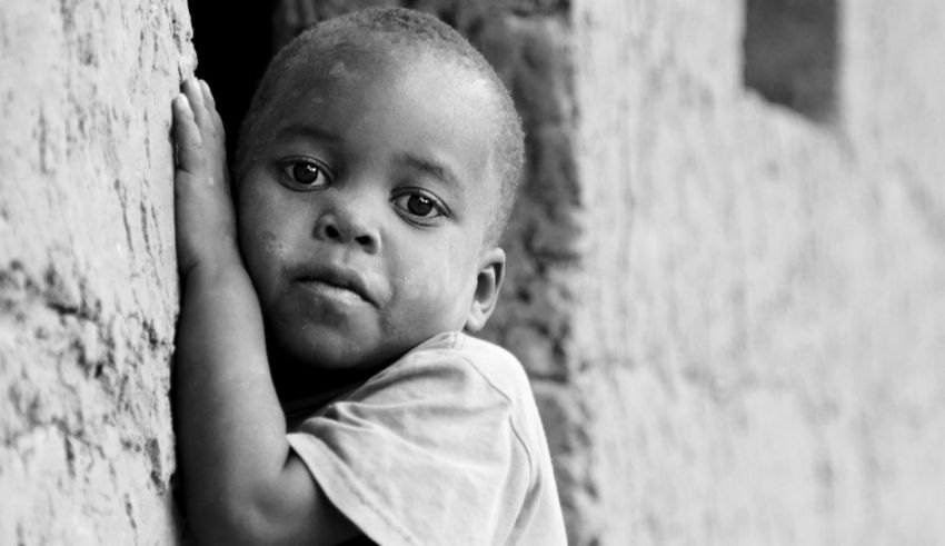 A black and white photo of a child leaning against a wall.