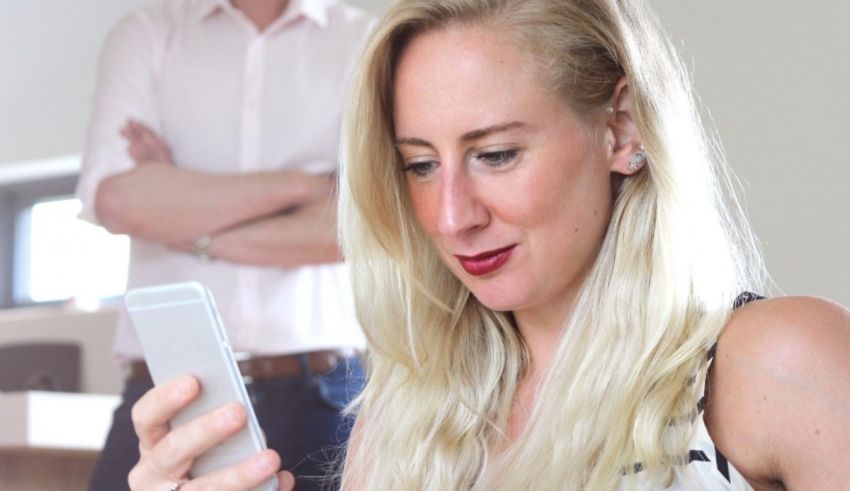 A woman looking at her cell phone in front of a man.