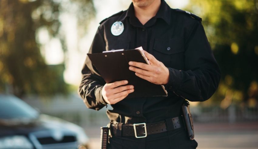 A police officer holding a clipboard in front of a car.