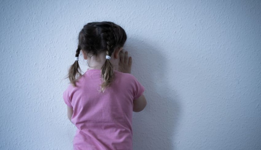 A little girl is standing in front of a white wall.
