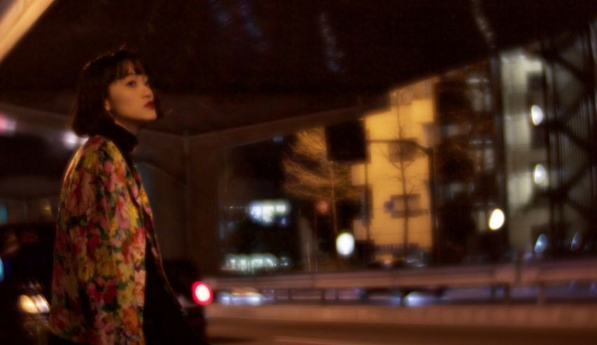 A woman in a floral jacket standing on a street at night.