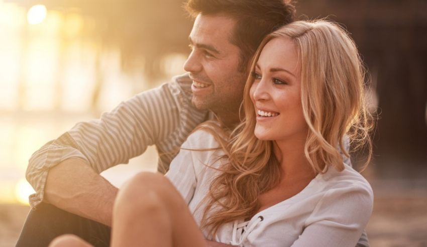 A man and woman sitting on the beach at sunset.