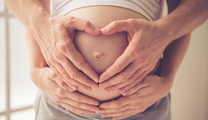 A pregnant woman is holding her belly with her hands.