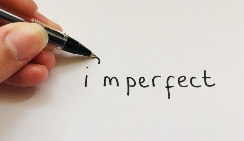 A person writing the word i imperfect on a piece of paper.