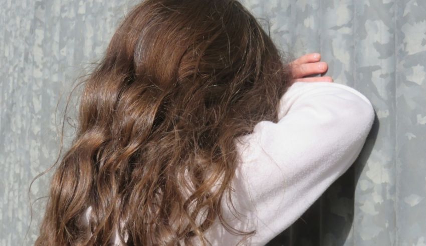 A girl with long hair leaning against a metal wall.