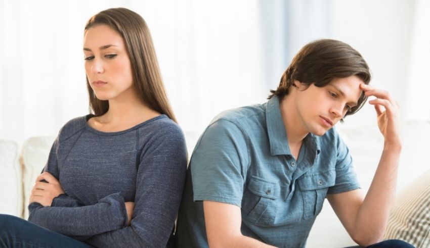 A man and woman sitting on a couch with their hands on their heads.