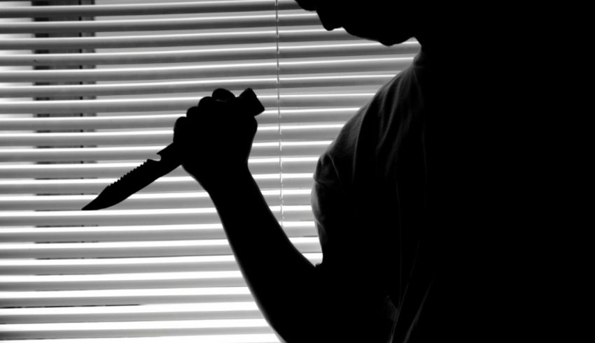 A silhouette of a man holding a knife in front of a window.