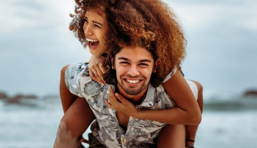 A young man is piggybacking a woman on the beach.