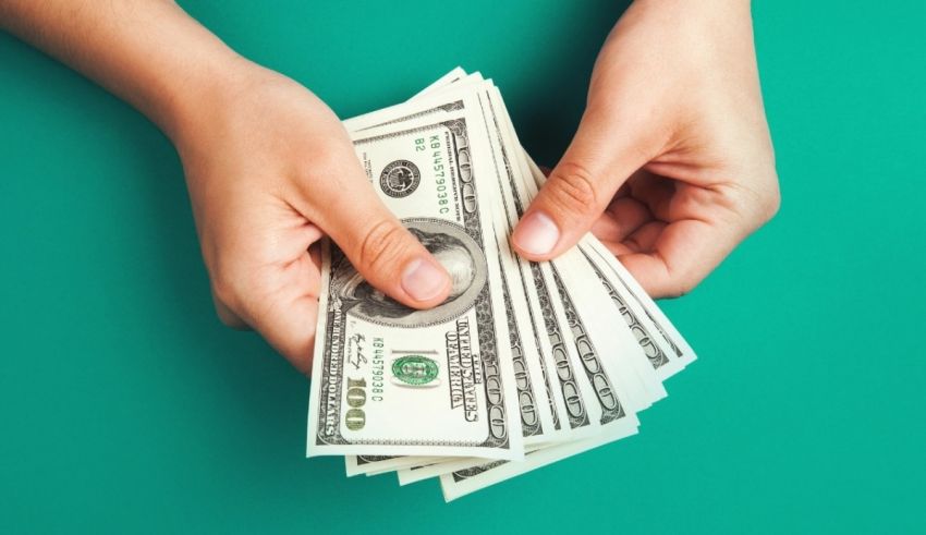 A woman's hand holding a stack of dollar bills on a green background.