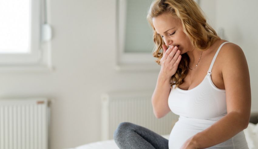 A pregnant woman sneezing while sitting on a bed.