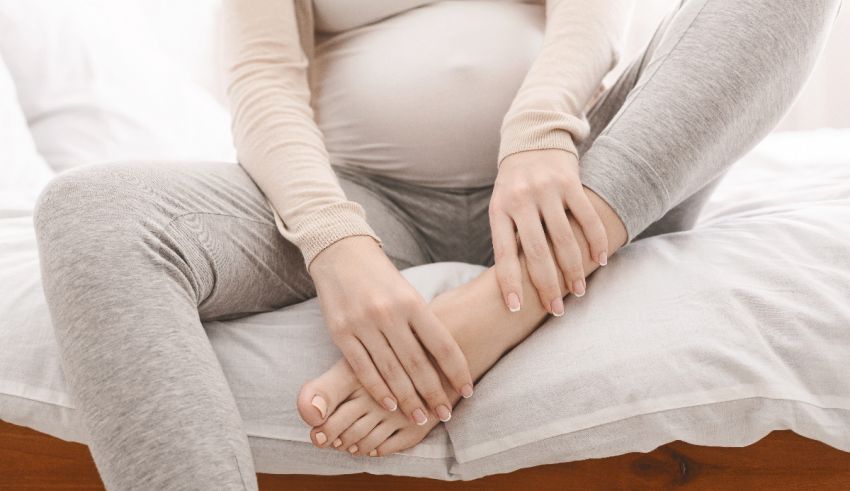 A pregnant woman sitting on a bed with her hands on her feet.