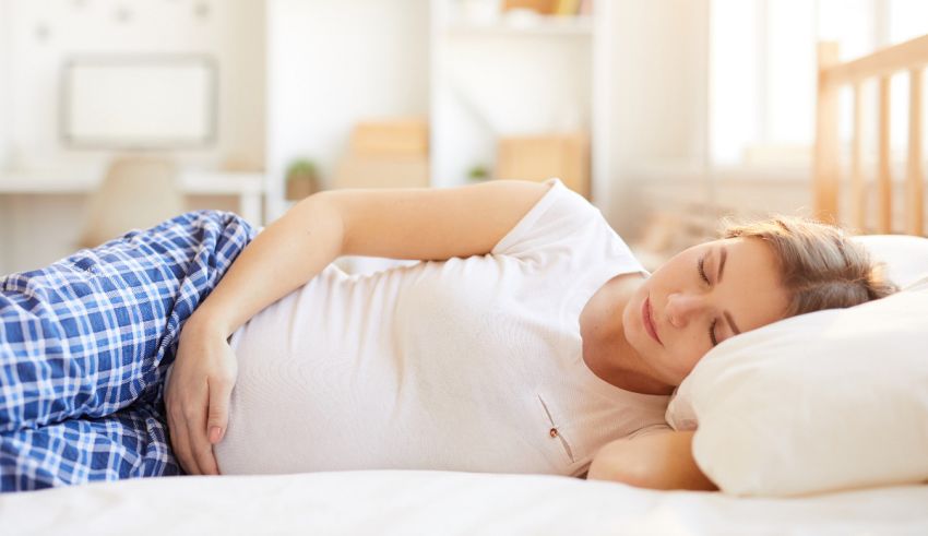 A pregnant woman laying on a bed with her hands on her stomach.