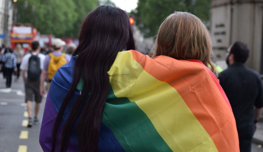 Two women walking down the street with a rainbow flag.