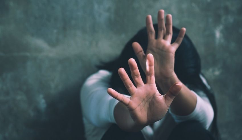 A woman with her hands up in front of a concrete wall.