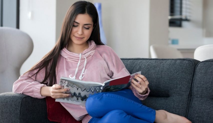 A young woman sitting on a couch reading a magazine.