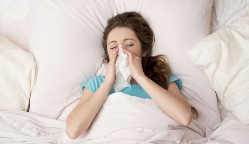 A woman sneezing in bed with a tissue.