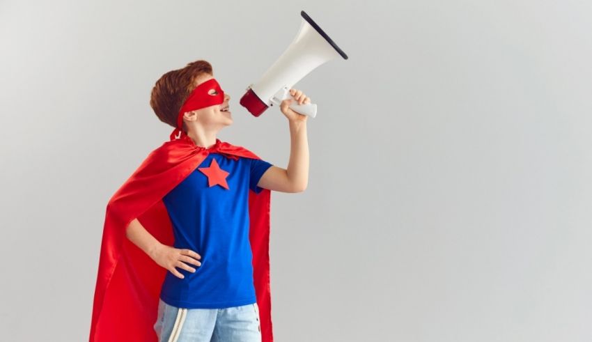 A young boy in a superhero costume shouting into a megaphone.