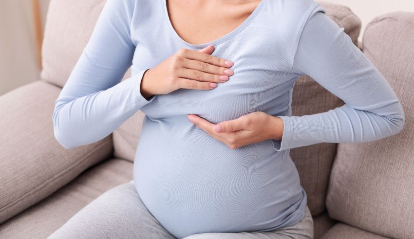 A pregnant woman holding her chest while sitting on a couch.