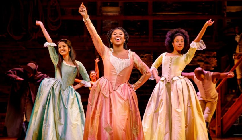 Three women in period dresses are dancing on stage.