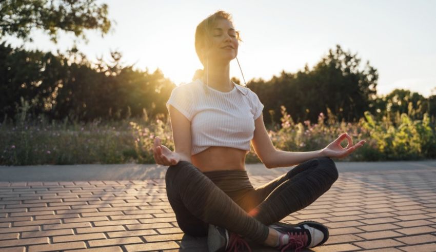 A woman is meditating outdoors at sunset.