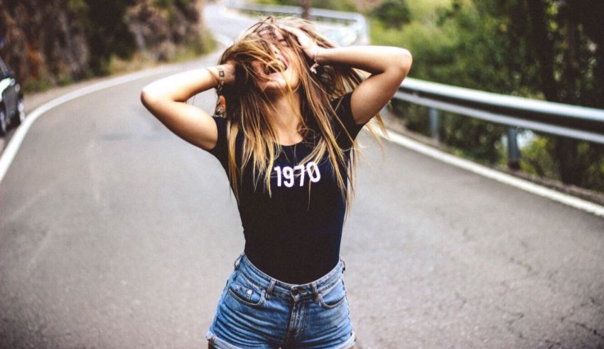 A girl in denim shorts and a t - shirt is standing on the side of a road.