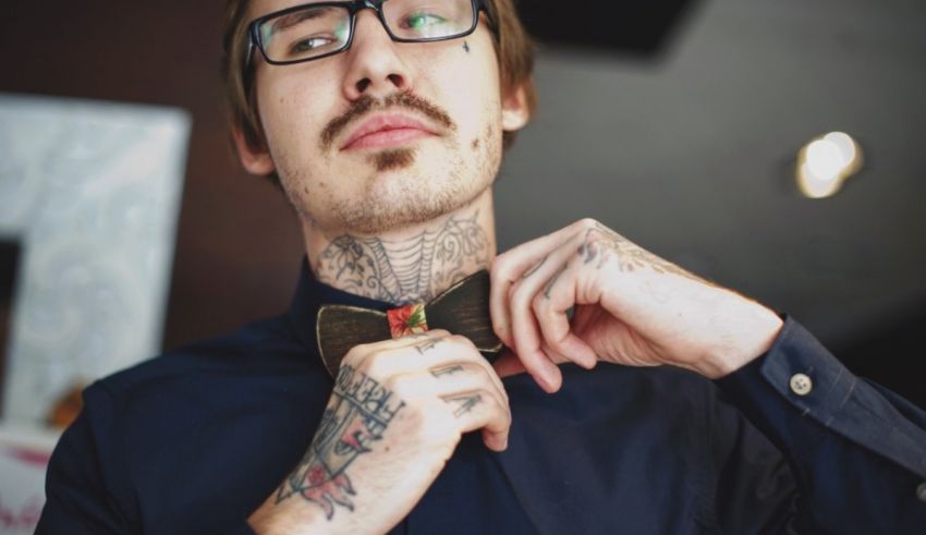 A man with tattoos adjusting his bow tie.