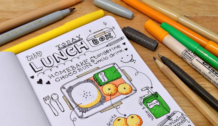 A notebook with pens, pencils, and food on it.