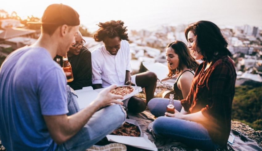 A group of friends sitting on a hill and eating pizza.