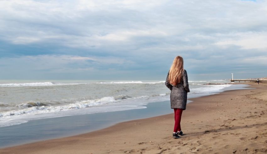 A woman is standing on a beach looking at the ocean.