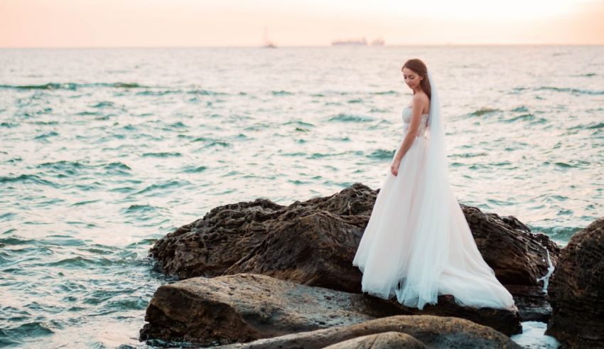 A bride in a wedding dress standing on rocks near the ocean.
