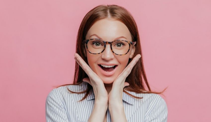 A woman wearing glasses and making a surprised face on pink background.