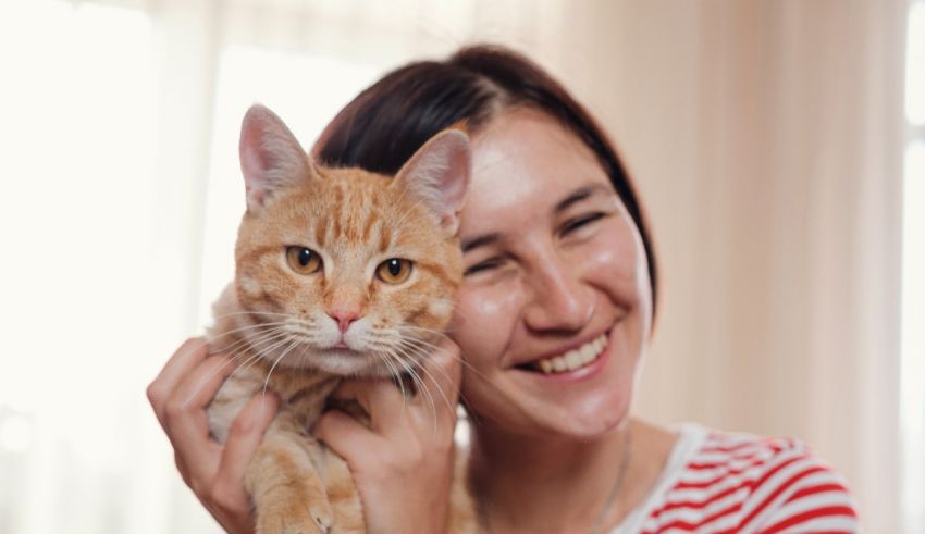 A woman smiles while holding an orange cat.