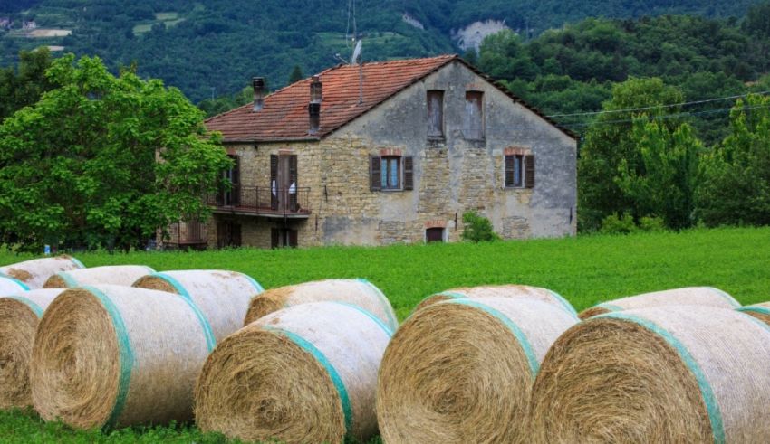 Hay bales in front of a house in the countryside.