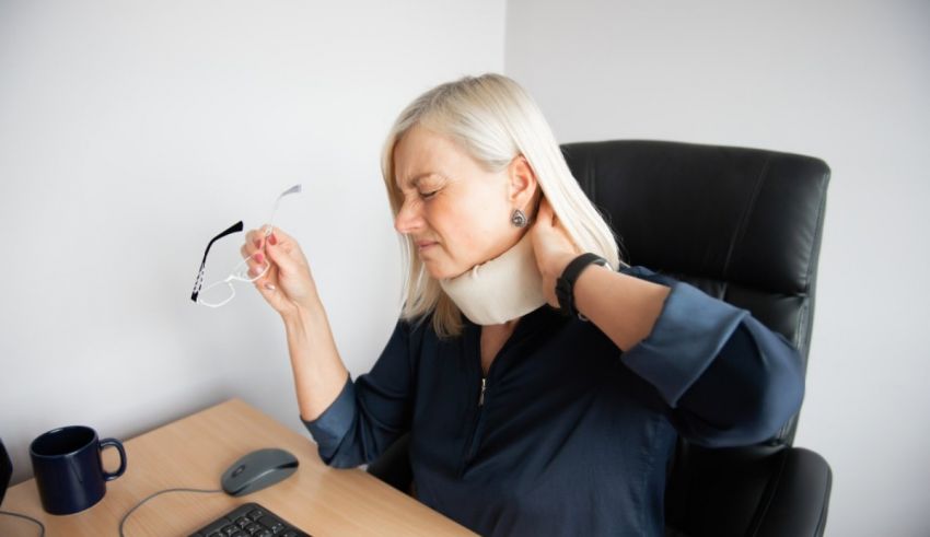 A woman with a neck pain is sitting at her desk.
