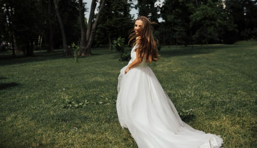A beautiful bride in a white wedding dress standing in a park.