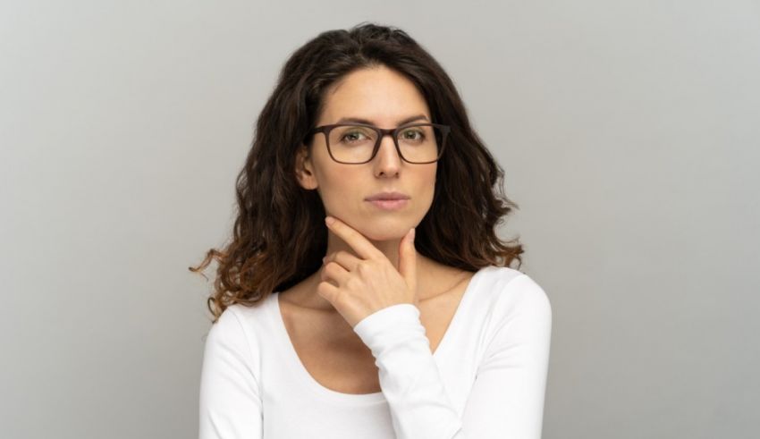 A woman in glasses is posing with her hand on her chin.