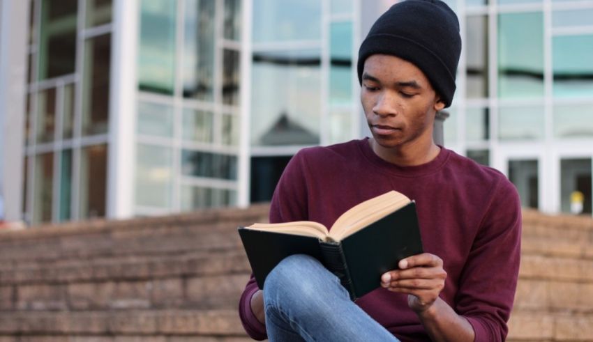 A young black man sitting on steps reading a book.
