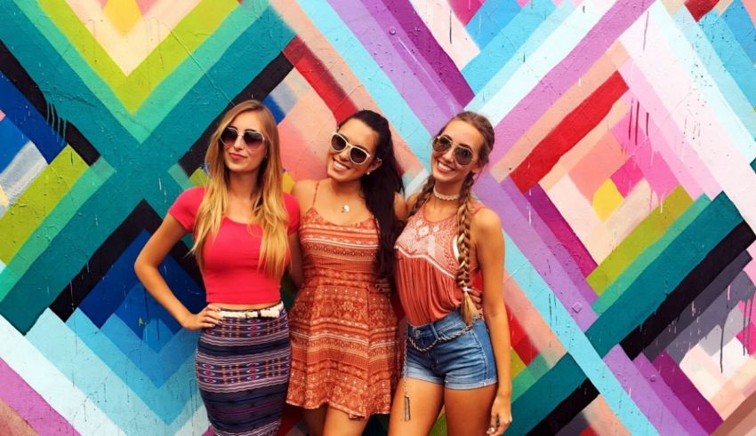 Three women posing in front of a colorful wall.