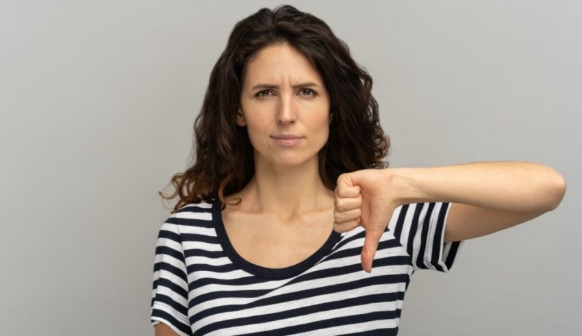 A woman showing a thumbs down sign on a gray background.