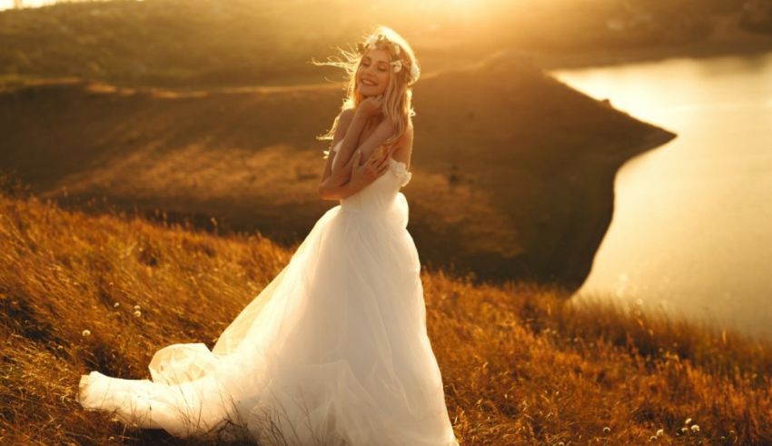 A bride in a wedding dress standing on a hill overlooking a lake.