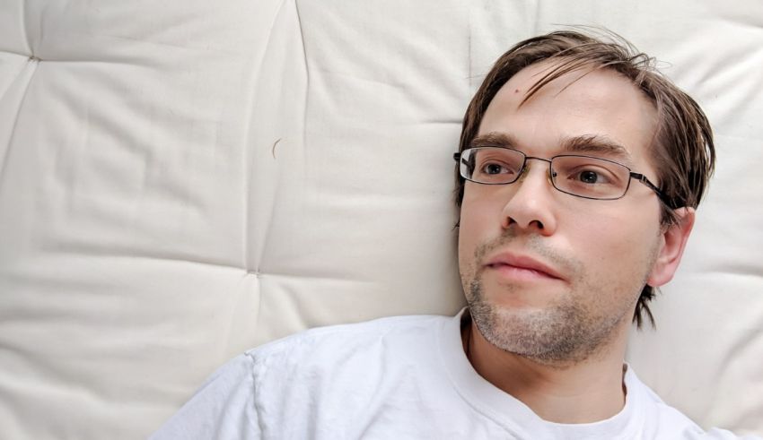 A man in glasses laying on a white bed.