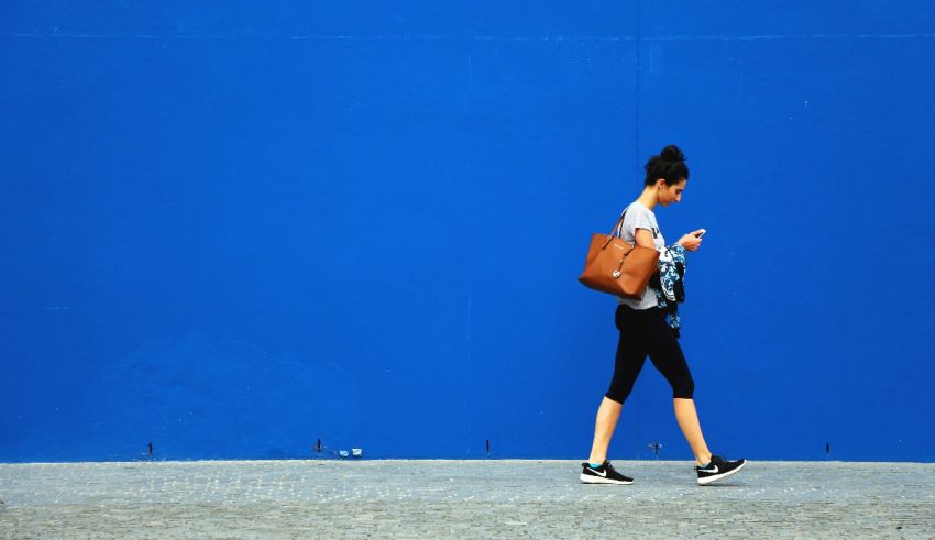 A woman walking down a street with a cell phone in her hand.