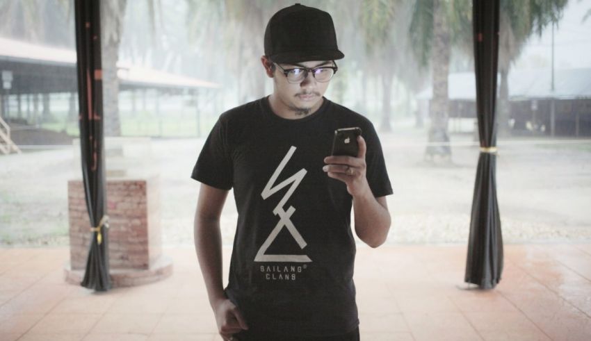 A man wearing glasses and a black t - shirt looking at his phone.