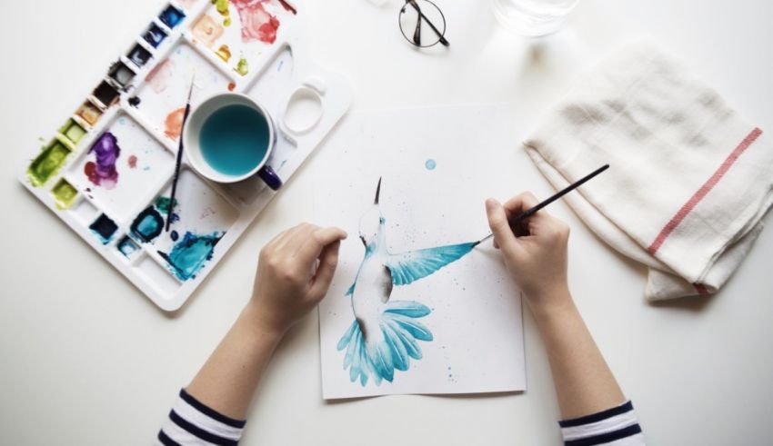 A woman is drawing a hummingbird on a piece of paper.