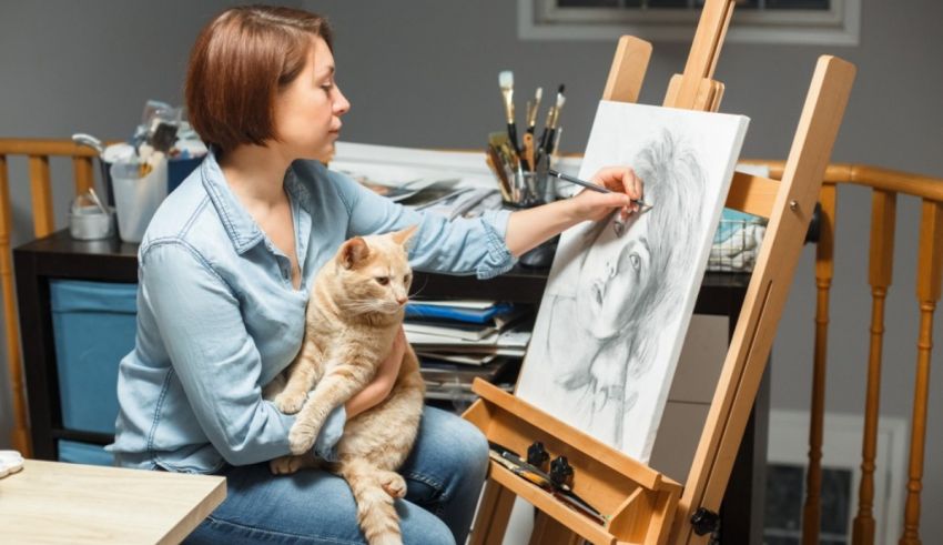 A woman is painting with her cat in front of an easel.