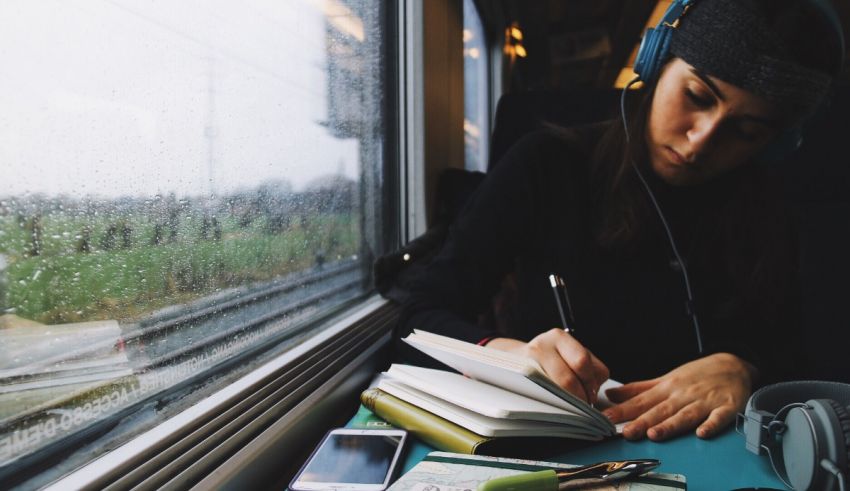 A woman sitting on a train with headphones and a notebook.