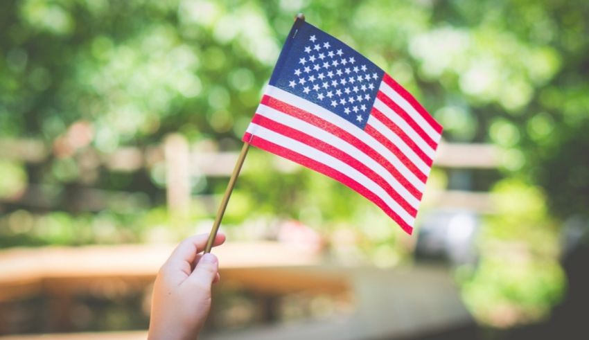 A person holding an american flag in front of a green background.