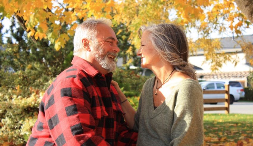 An older couple in a plaid shirt standing under a tree.